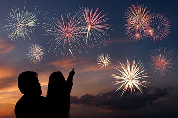 Father and daughter pointing at fireworks in the night sky.