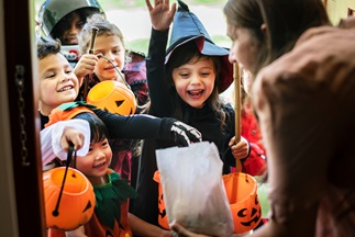 Kids in costumes trick or treating and grabbing candy out of a white bag
