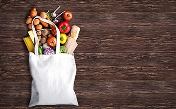 Canvas bag of groceries against a wood panel background with fruits, vegetables and grains coming out the top of the bag.
