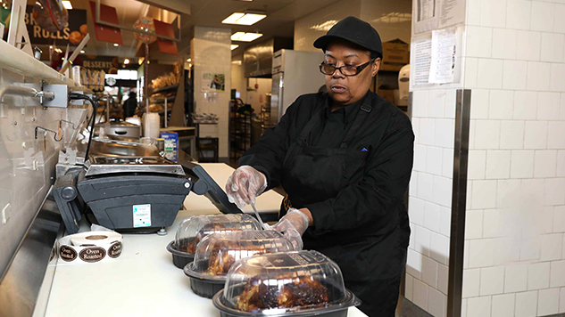 Food safety worker putting labels on rotisserie chicken in packaging.